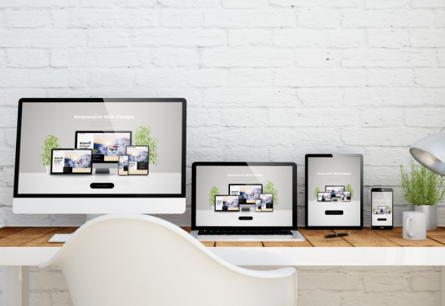 Mockup of a responsive web site displayed on a monitor, laptop, tablet and phone sitting alongside one another of a wooden desk.
